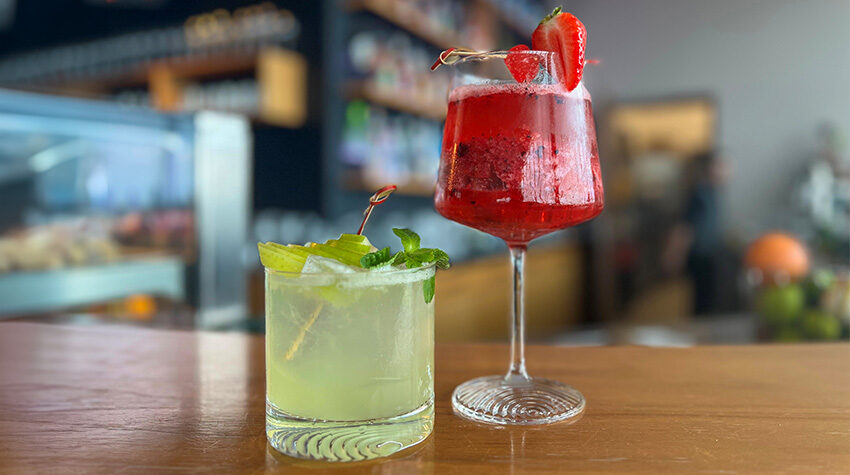 Zwei alkoholfreie Cocktails. Einer in einem Longdrinkglas und in minzgrün, ein anderer in einem hohen Glas mit Erdbeeren.