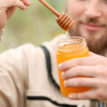 Ein Imker, der ein Glas Honig mit einem Honiglöffel in der Hand hält. ©Adobe Stock, Pixel-Shot