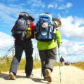 Zwei Personen mit Rucksäcken wandern einen Weg entlang.
