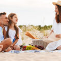 Familie genießt ein gemeinsames Picknick mit Burgern und Limo am Strand der Ostsee.
