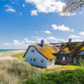 Reetdachhaus an der Ostseeküste mit Blick auf Strand, Dünen und das türkis schimmernde Meer bei Sonnenschein.