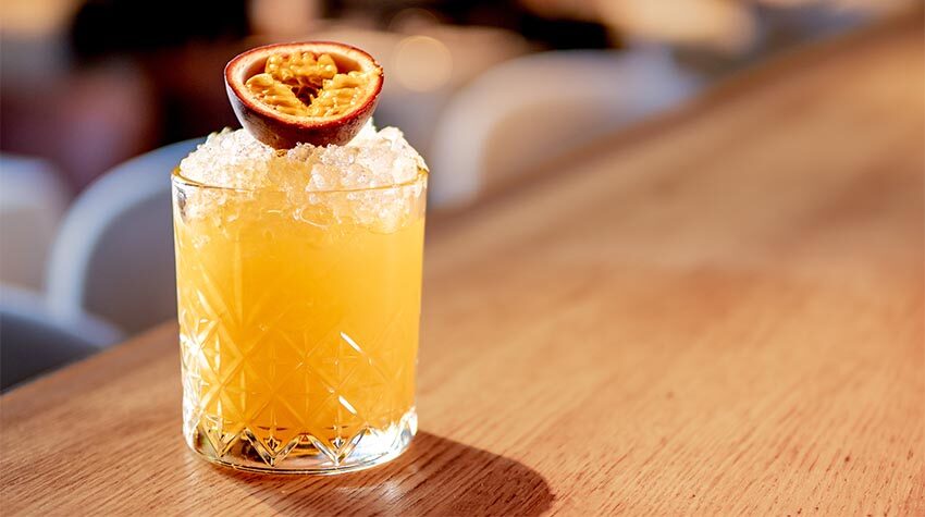 Cocktail mit Passionsfrucht, serviert auf einem Holzbrett.