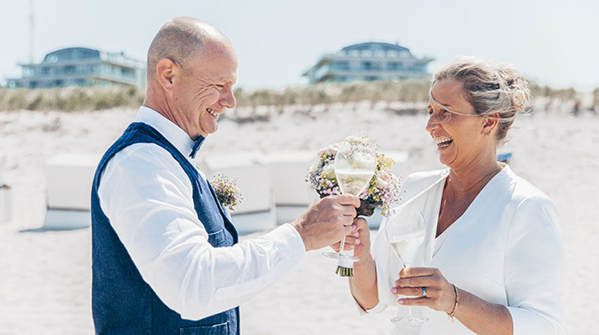 Glückliches Ehepaar stößt am Ostseestrand mit Sekt an.