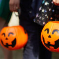 Kinder mit Halloween-Kürbiseimern gehen verkleidet von Haus zu Haus, um Süßigkeiten zu sammeln.