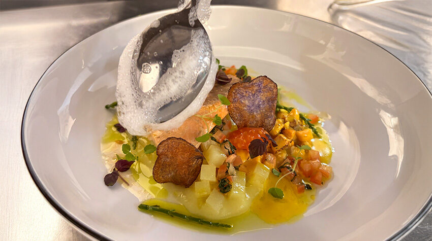 Küchenchef im SEASIDE des THE GRAND Ahrenshoop setzt Schaum auf ein Saiblingsgericht mit Gemüse und Kräutern.