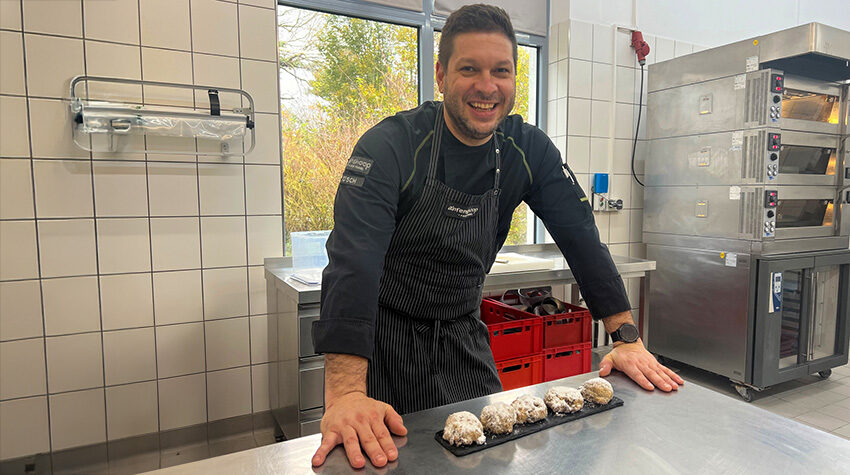 Stefan Lösch steht in einer hellen Backstube vor einem Blech mit frisch zubereitetem Stollenkonfekt.