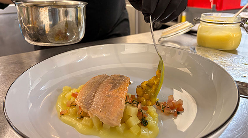 Anrichten eines Saiblings im SEASIDE des THE GRAND Ahrenshoop mit Gemüsewürfeln, Kräutern und aufgeschäumter Sauce.