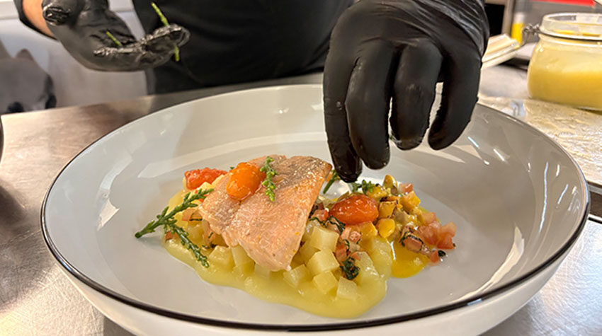 Saiblingsfilet im SEASIDE des THE GRAND Ahrenshoop wird mit Öl und Kräutern finalisiert.