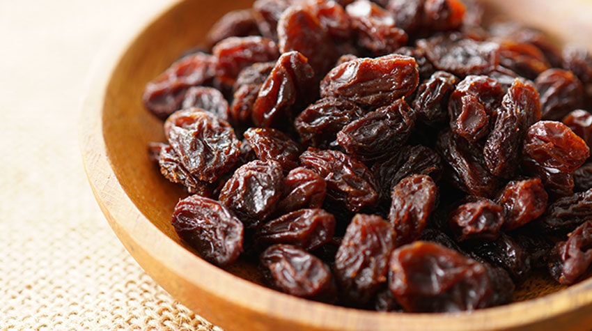 Nahaufnahme einer Schale voller dunkler, saftiger Rosinen auf hellem Untergrund.