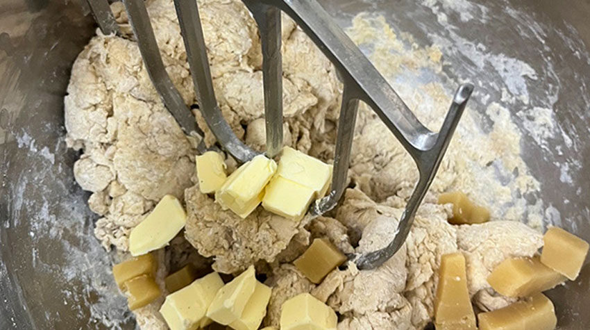 Teig für einen Stollen in einer Rührschüssel, in den kleine Butterwürfel eingearbeitet werden.