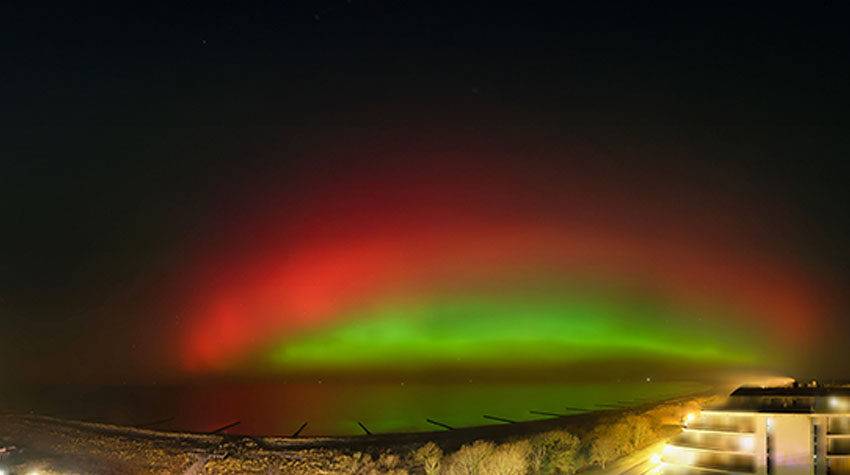 Rot-grüne Polarlichter leuchten über der Ostsee bei Ahrenshoop in der Nacht.