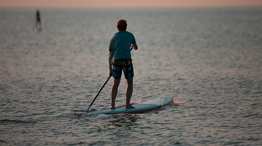 Person steht auf einem Stand-Up-Paddle-Board auf der ruhigen Ostsee.