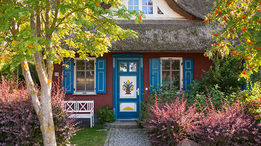 Reetgedecktes Haus mit farbiger Haustür und Garten im Ostseeort Ahrenshoop an der Küste von Fischland-Darß-Zingst.