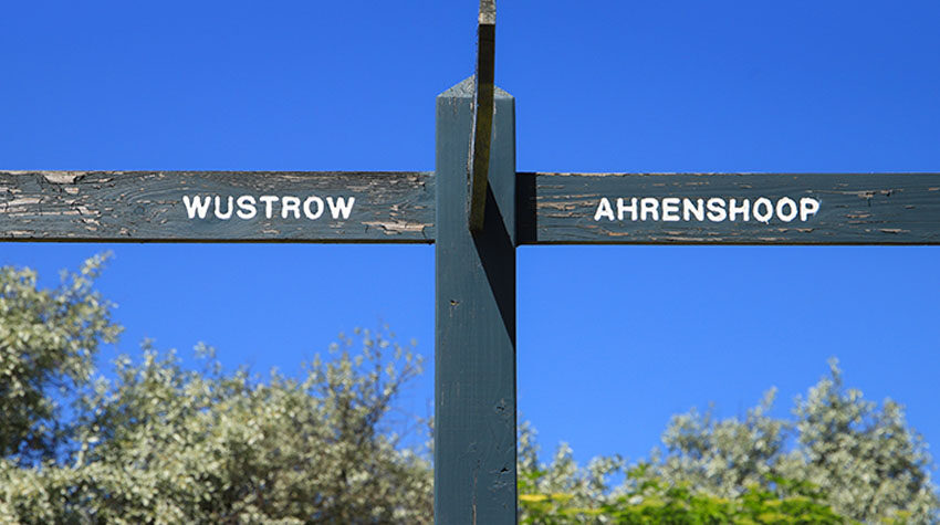 Wegweiser zwischen Wustrow und Ahrenshoop auf dem Fischland-Darß mit blauem Himmel und Dünenvegetation.
